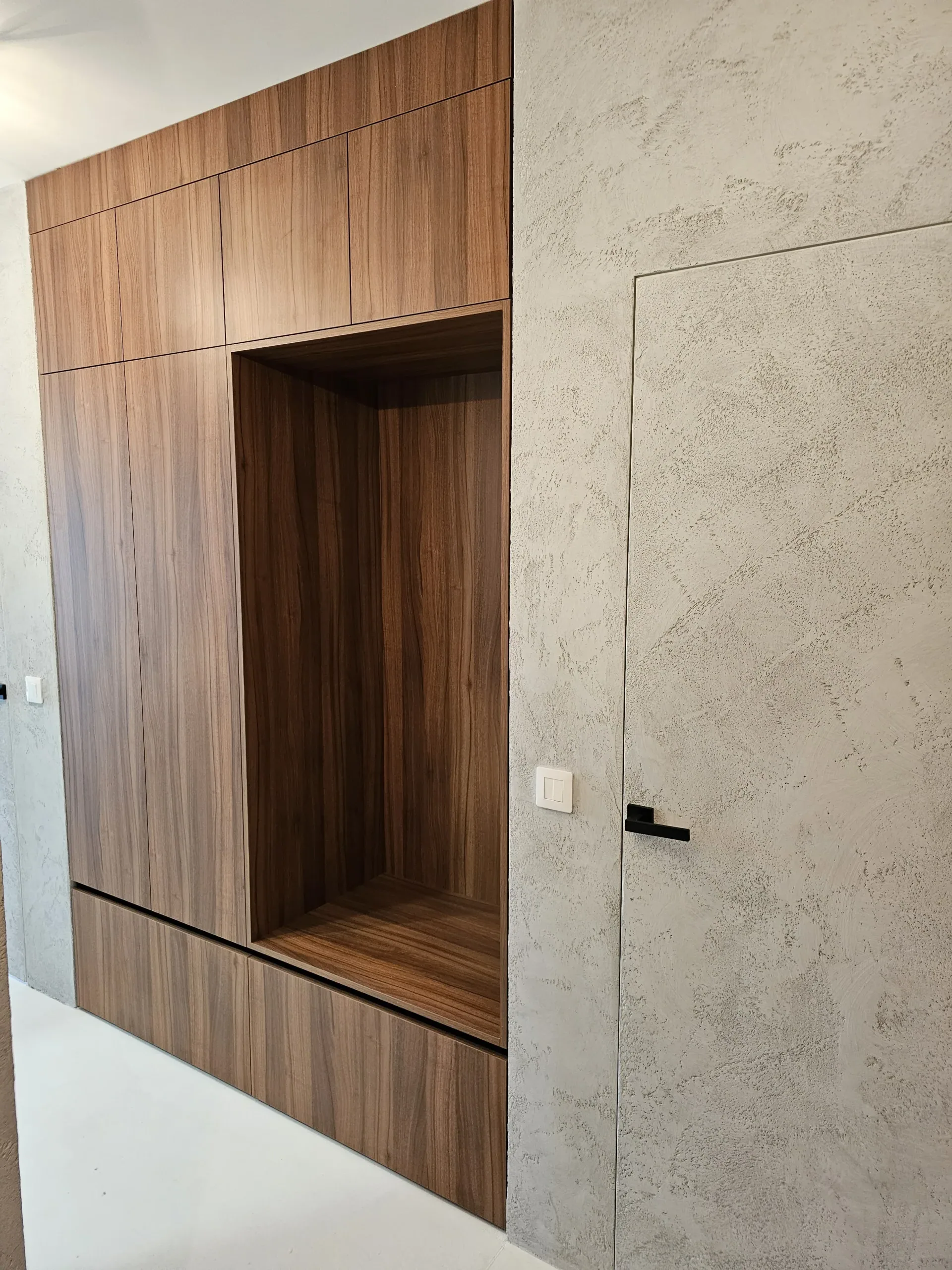 Ugrađeni drveni ormar sa sjedećom nišom uz dekorativni zid prekriven sivom žbukom.